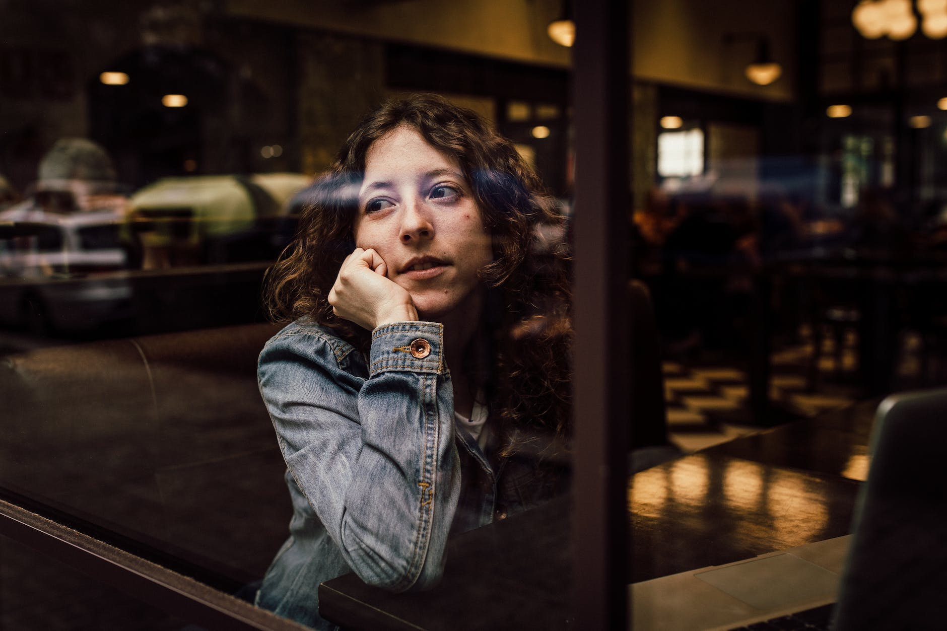 woman wearing blue denim jacket putting her right arm on her cheek