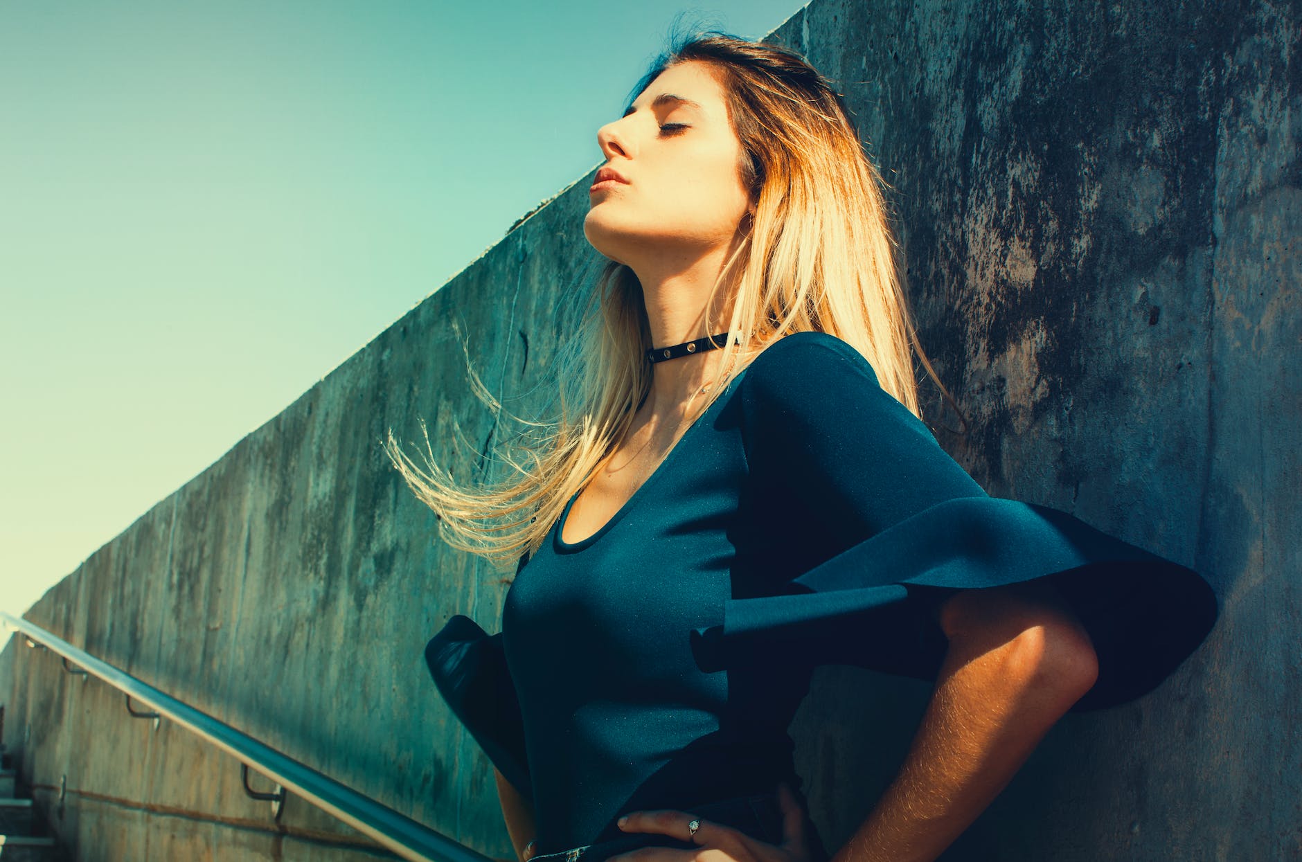 woman wearing blue scoop neck top standing near gray concrete wall
